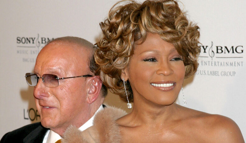 Whitney Houston surâzătoare cu o blană bej pe un umăr și cu o rochie aurie care îi pune în valoare bustul generos înainte de a fi printre cei 3 artiști care s-au înecat