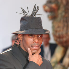 Coolio este la o prezentare de modă și are pe cap o pălărie neagră cu pene la spate. Este unul dintre artiștii care au murit pe scenă.