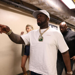 50 Cent a rănit o femeie după ce a aruncat cu microfonul în mulțime. Rapperul poartă un tricou alb și o șapcă albă. Arată cu degetul spre fani