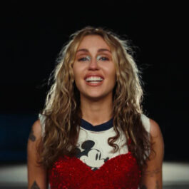 Miley Cyrus și-a schimbat culoarea părului. Aici este cu buclele blonde și poartă un tricou roșu cu partea de sus albă. Pe bucata albă este Mickey Mouse