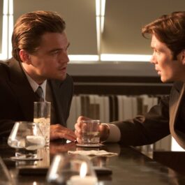 Filmul în care joacă Cillian Murphy și Leonardo DiCaprio este în top 20 cele mai bune filme din toate timpurile. Cei doi stau la o masă și discută. Pe masă sunt mai multe pahare și șervețele.