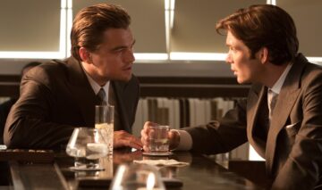Filmul în care joacă Cillian Murphy și Leonardo DiCaprio este în top 20 cele mai bune filme din toate timpurile. Cei doi stau la o masă și discută. Pe masă sunt mai multe pahare și șervețele.