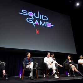 Actorii din primul sezon Squid Game cu numele emisiunii deasupra lor pe un ecran imens