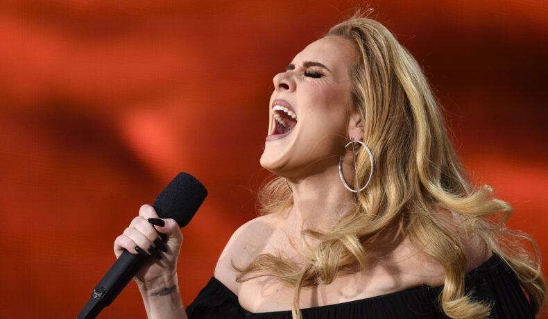 Adele cu unghii negre și un tatuaj pe încheietură ținând microfonul și cântand