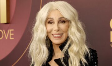Cher machiată cu părul blond și îmbrăcată cu o rochie neagră