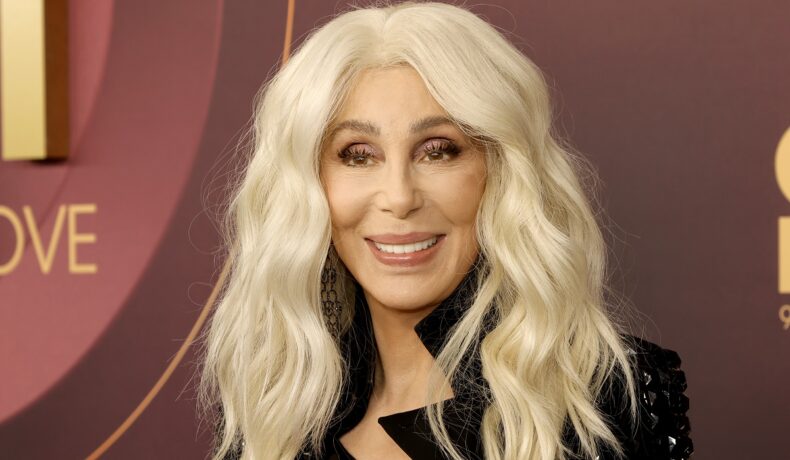 Cher machiată cu părul blond și îmbrăcată cu o rochie neagră