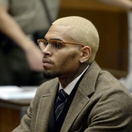 Chris Brown îmbrăcat într-un costum maro cu părul blond si ochelari asortați
