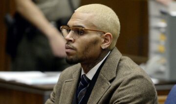 Chris Brown îmbrăcat într-un costum maro cu părul blond si ochelari asortați