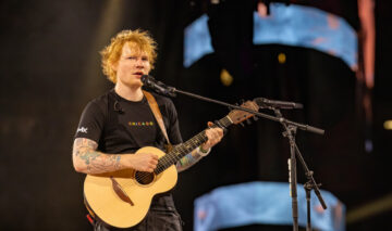 Ed Sheeran și-a acordat o mărire de salariu de 10 milioane de lire sterline. Aici este pe scenă și cântă în fața publicului din Chicago. Are pantaloni cargo negri și un tricou negru
