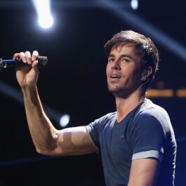 Enrique Iglesias îmbrăcat cu un tricou albastru în timp ce ține un microfon în mâna dreptă