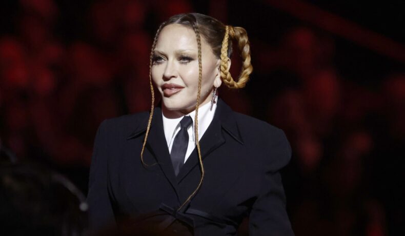 Madonna, cu o coafură excentrică din două cozi împletite, îmbrăcată în cămașă albă cu cravata și sacou negru
