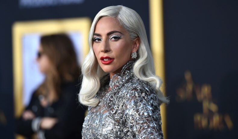 Lady Gaga fotografiată într-o rochie argintie și cu părul de culoare blond platinat care este ondulat