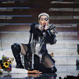 Madonna, pe scenă, în timpul unui concert, cu o ținută excentrică, cu multe lanțuri, corset și cizme înalte din piele