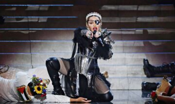 Madonna, pe scenă, în timpul unui concert, cu o ținută excentrică, cu multe lanțuri, corset și cizme înalte din piele