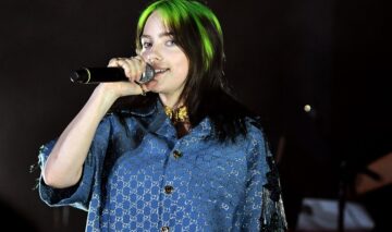 Billie Eilish vopsită în două culori în timp ce cântă la microfon