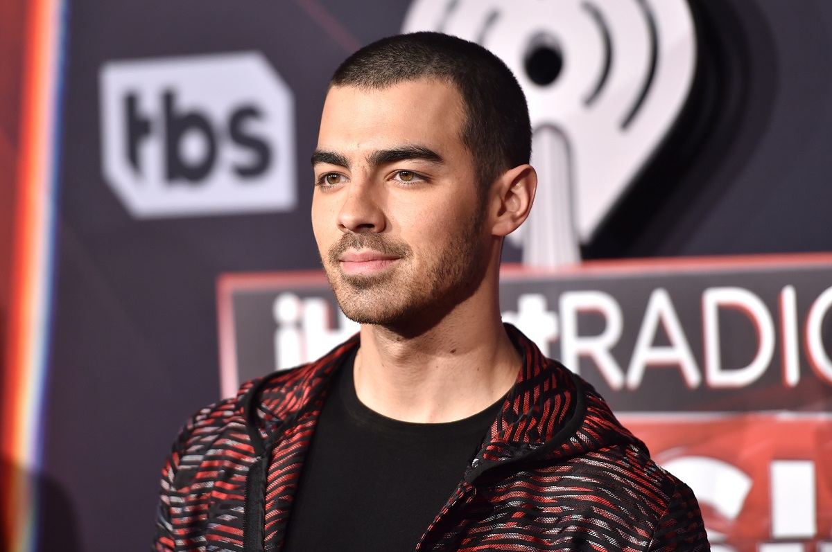 Joe Jonas tuns scurt purtând un tricou negru și o bluză de training
