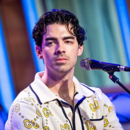 Joe Jonas stând în fața microfonului îmbrăcat într-un un tricou polo alb