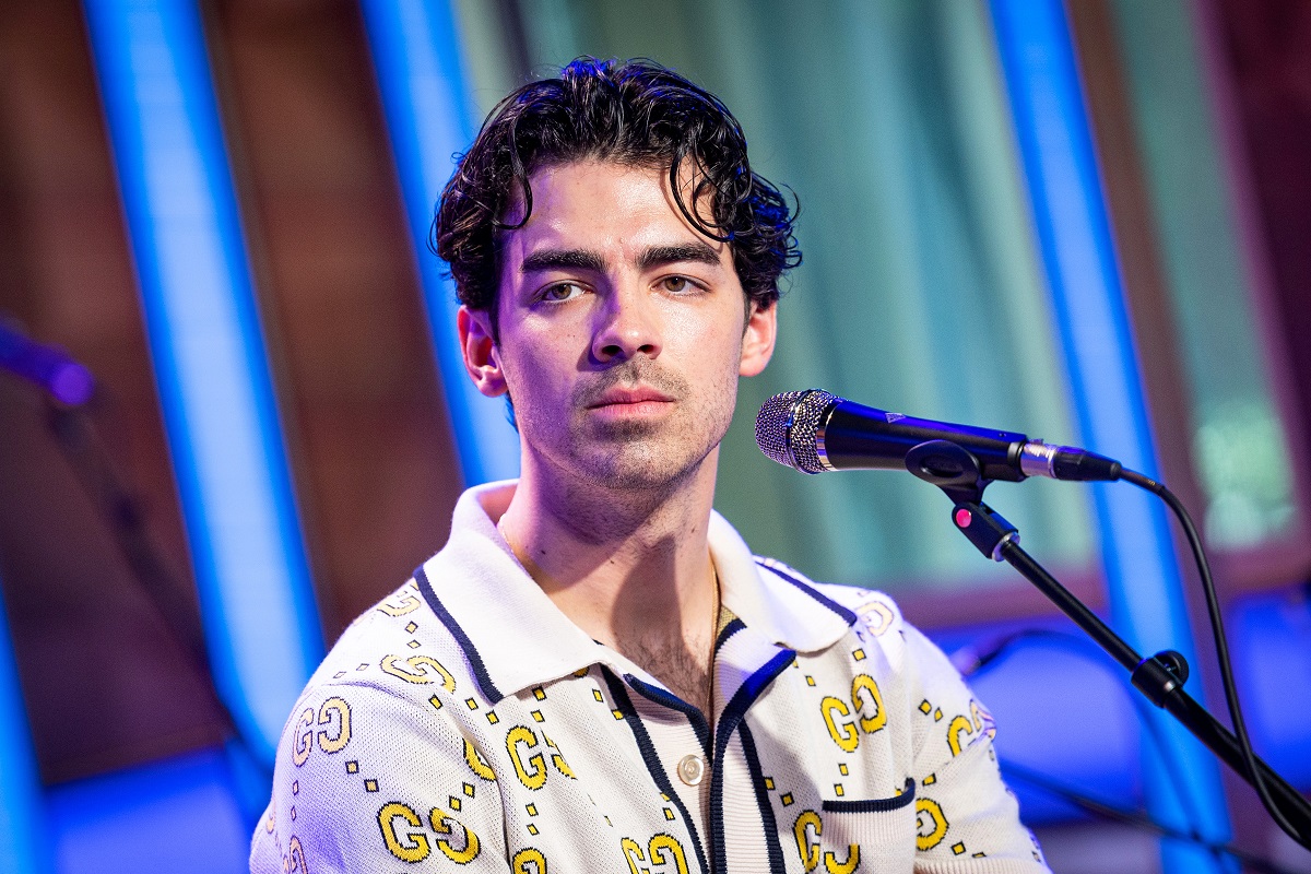 Joe Jonas stând în fața microfonului îmbrăcat într-un un tricou polo alb