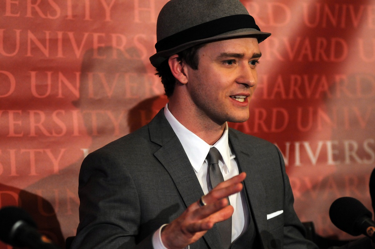 Justin Timberlake îmbrăcat elegant cu o pălărie în cap în timp ce vorbește la microfon