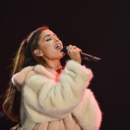 Ariana Grande îmbrăcată într-o haină de blană pufoasă în timp ce cântă la microfon