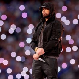 Eminem îmbrăcat cu un hanorac negru și o șapcă în timp ce ține microfonul în mână