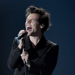 Harry Styles îmbrăcat în negru în timp ce cântă la microfon