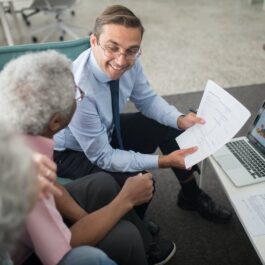 Un bărbat care stă în fața unui laptop și discută cu doi angajați