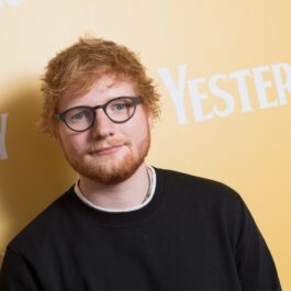 Ed Sheeran îmbrăcat cu o bluză neagră purtând ochelari rotunzi cu ramă neagră