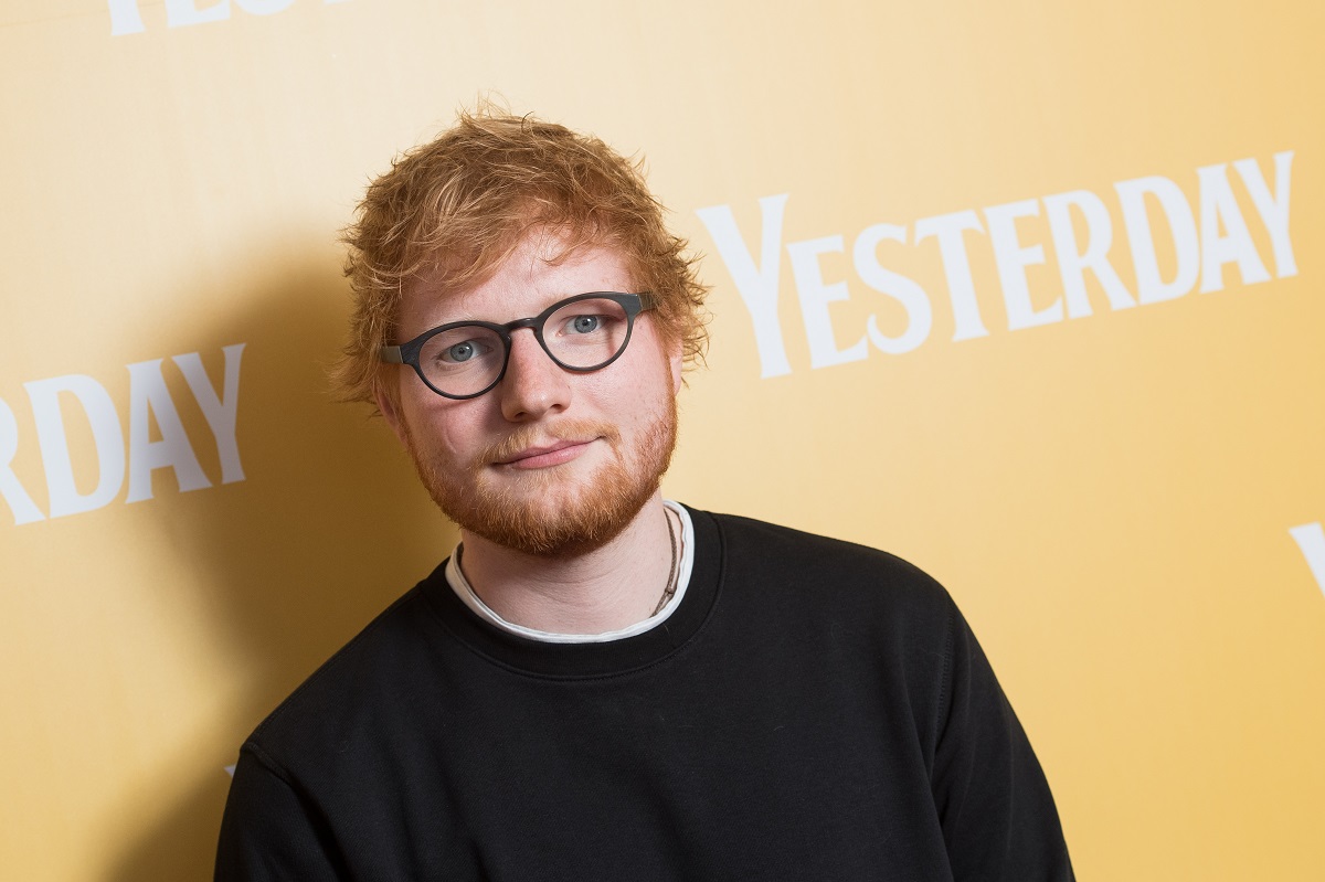 Ed Sheeran îmbrăcat cu o bluză neagră purtând ochelari rotunzi cu ramă neagră