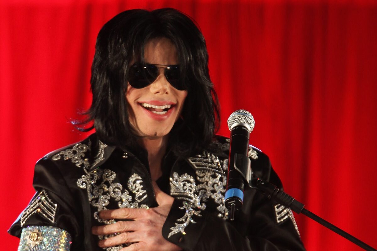 Michael Jackson purtând ochelari de soare și îmbrăcat cu ținută neagră care prezintă ornamente argintii strălucitoare