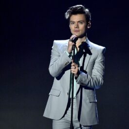 Harry Styles îmbrăcat într-un costum gri în timp ce cântă la microfon