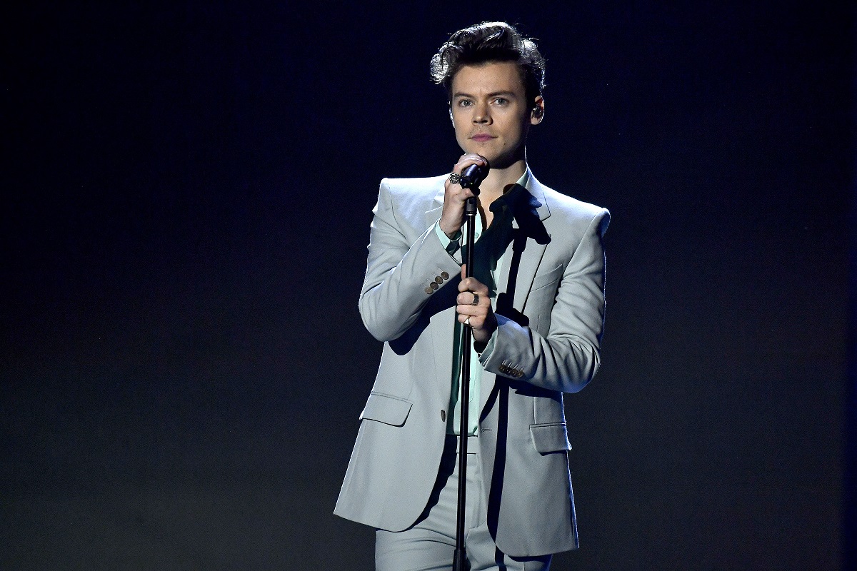 Harry Styles îmbrăcat într-un costum gri în timp ce cântă la microfon