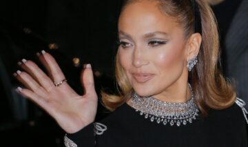 Jennifer Lopez îmbrăcată într-o ținută neagră cu un colier argintiu în timp ce gesticulează un salut din mână