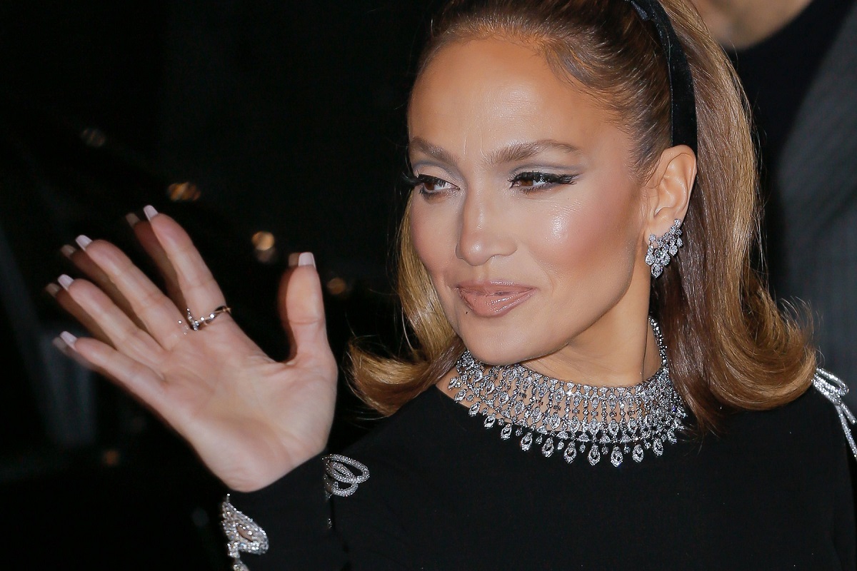 Jennifer Lopez îmbrăcată într-o ținută neagră cu un colier argintiu în timp ce gesticulează un salut din mână