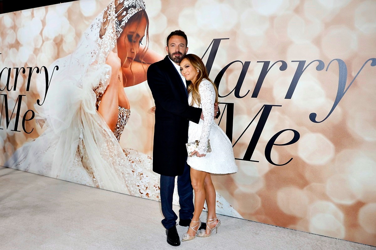Ben Affleck îmbrăcat într-un costum negru în timp ce o ține în brațe pe Jennifer Lopez care este îmbrăcată într-o rochie albă