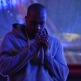 Kanye West îmbrăcat într-un hanorac în timp ce cântă cu microfonul apropiat de gură