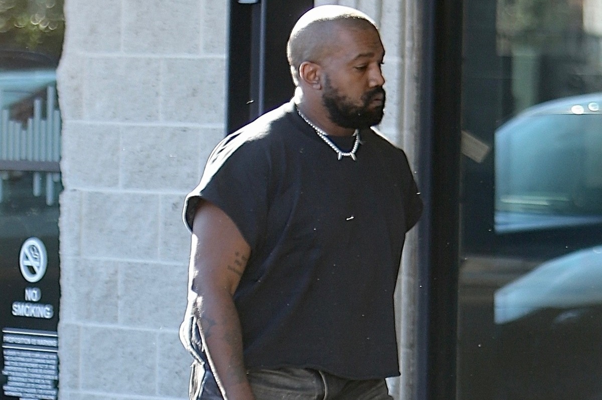 Kanye West îmbrăcat cu un tricou negru accesorizat cu un lanț argintiu în timp ce merge