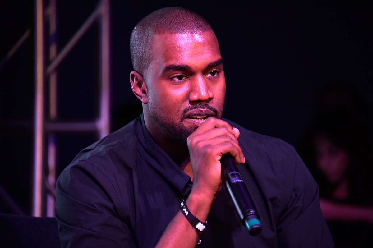 Kanye West îmbrăcat într-o cămașă neagră în timp ce vorbește la microfon