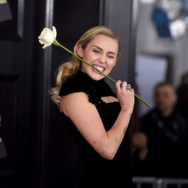 Miley Cyrus îmbrăcată într-o rochie neagră în timp ce ține un trandafir alb în gură