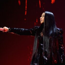 Nicki Minaj îmbrăcată într-o ținută neagră strălucitoare din piele în timp ce ține un microfon în mână