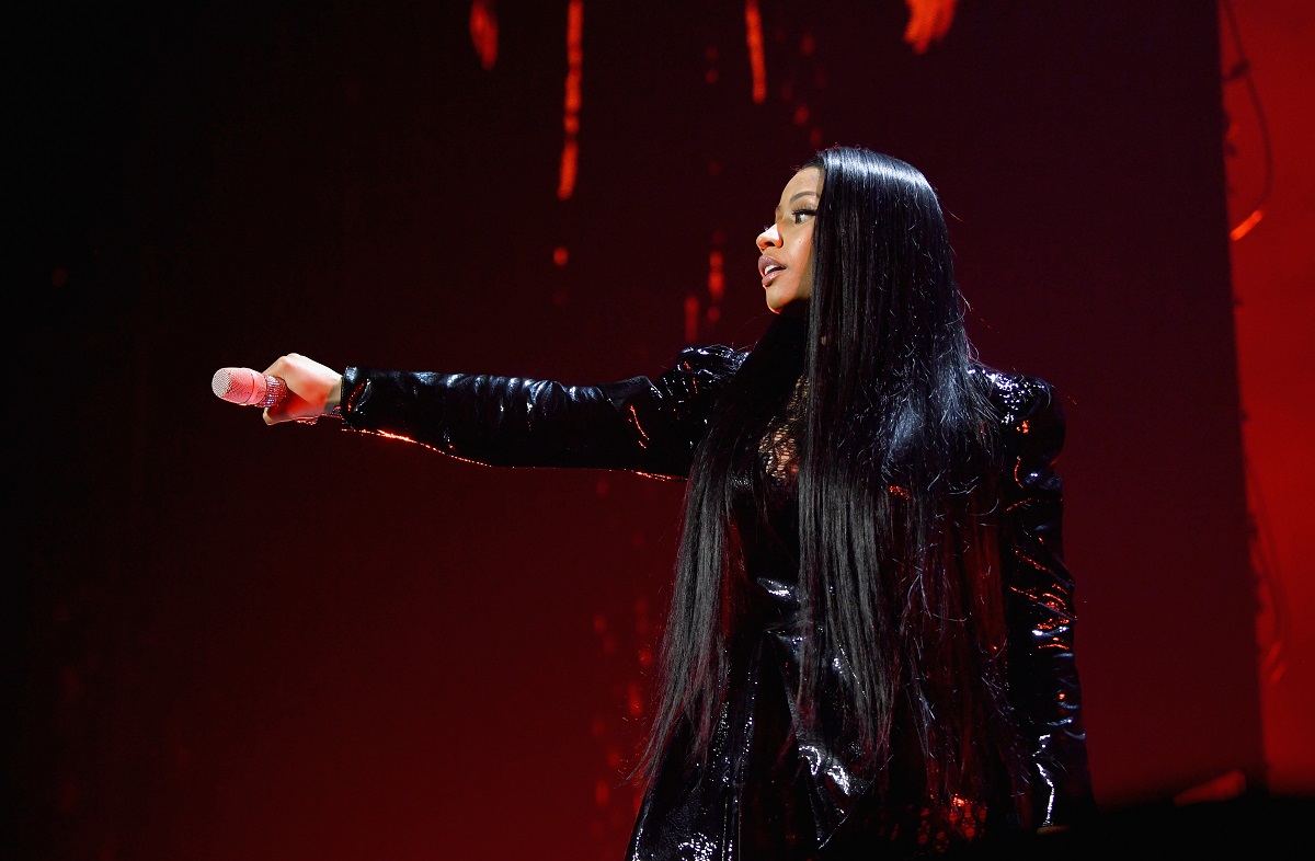 Nicki Minaj îmbrăcată într-o ținută neagră strălucitoare din piele în timp ce ține un microfon în mână