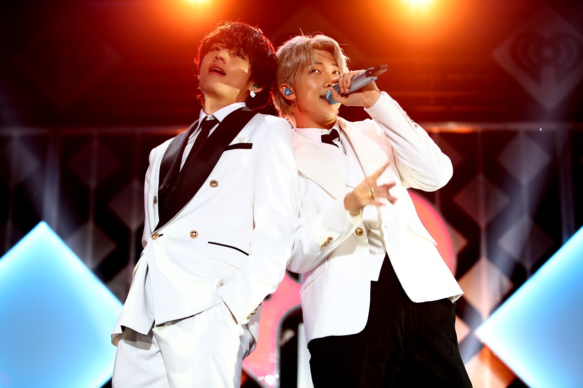 RM și V îmbrăcați în costume albe în timp ce stau spate în spate și cântă la microfon