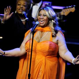 Aretha Franklin îmbrăcată într-o rochie portocalie în timp ce cântă la microfon