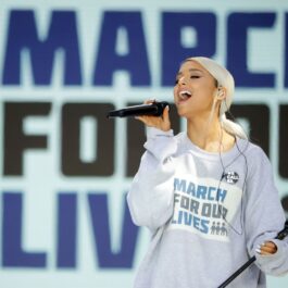 Ariana Grande îmbrăcată într-un hanorac albastru deschis în timp ce cântă la microfon