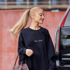 Ariana Grande îmbrăcată casual cu o bluză neagră largă și blugi în timp ce merge și ține o geantă în mână