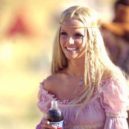Britney Spears îmbrăcată într-o rochie roz în timp ce ține o sticlă de suc în mână
