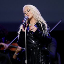 Christina Aguilera îmbrăcată într-un halat negru lucios în timp ce cântă la microfon