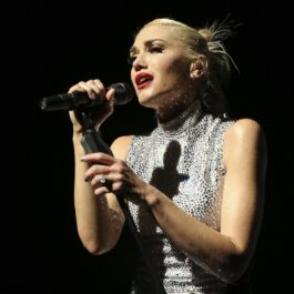Gwen Stefani îmbrăcată intr-o rochie albă cu buline negre fără umeri în timp ce cântă la microfon