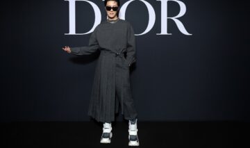 J-Hope îmbrăcat într-o ținută neagră în fața unui perete pe care scrie Dior