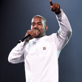 Kanye West îmbrăcat într-o ținută albă în timp ce cântă la microfon